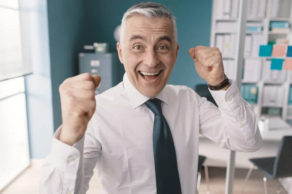 笑容满面的商人举起拳头庆祝他在办公室的成功 — 图库照片