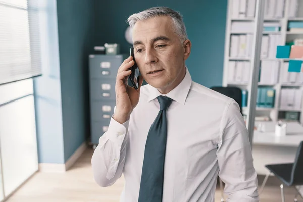 彼のオフィスに立って 彼のスマートフォンで電話を持っているエグゼクティブ — ストック写真