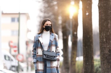 Koruyucu yüz maskesi takan ve sokakta yürüyen genç bir kadın.