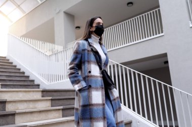 Yüz maskesi takan ve merdivenlerden inen genç bir kadın, koronavirüs önleme konsepti.