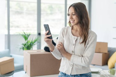 Yeni evinde akıllı telefonuyla iletişim kuran mutlu bir kadın arkadaşlarını arıyor.
