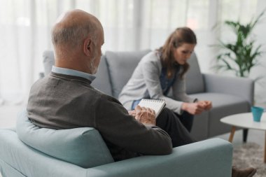 Terapi seansı sırasında depresyondaki kadın konuşuyor, psikolog notlar yazıyor ve dinliyor.