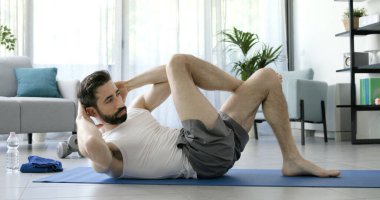 Evdeki egzersiz paspasında çalışan bir adam karın kaslarını çalıştırıyor.