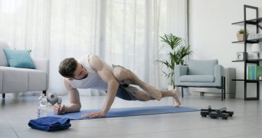 Kaslı adam evde çalışıyor, yerde egzersiz yapıyor, spor yapıyor ve spor yapıyor.