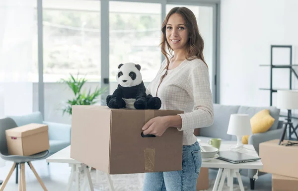 幸せな若い女性は彼女の新しい家に移動し 彼女は段ボール箱とパンダのぬいぐるみを運んでいる — ストック写真