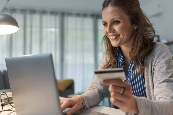Masada Oturmuş Gülümseyen Genç Bir Kadın Internetten Kredi Kartı Kullanıyor — Stok fotoğraf