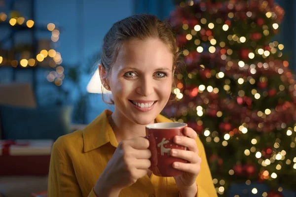 家でクリスマスを祝う幸せな若い女性 彼女は熱いお茶を飲んでいます — ストック写真