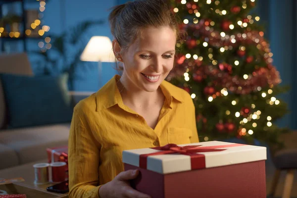 幸せな女性座っています上のソファに家とオープン彼女のクリスマスプレゼント — ストック写真