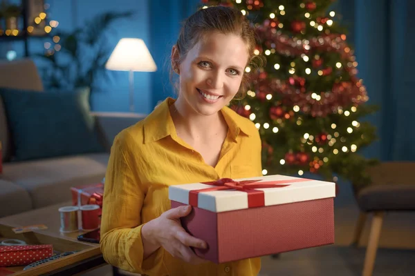 幸せな女性はソファに座ってクリスマスプレゼントを持って 彼女はカメラで笑っています — ストック写真