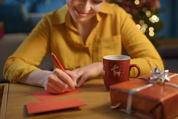 幸せな女性はクリスマスカードを書き 彼女の友人のためのギフトを準備する — ストック写真