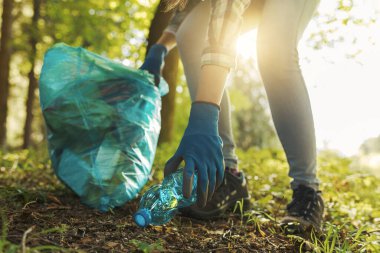 Temizlik gönüllüsü ormanda çöp topluyor ve bir çöp torbası tutuyor. Çevre koruma kavramı.
