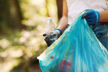 Temizlik gönüllüsü bir çöp torbası tutuyor ve ormanda çöp topluyor.
