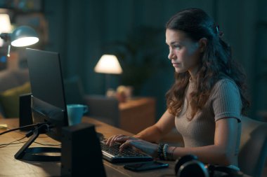 Geceleri evden çalışan genç bir kadın, bilgisayarına bağlanıyor.