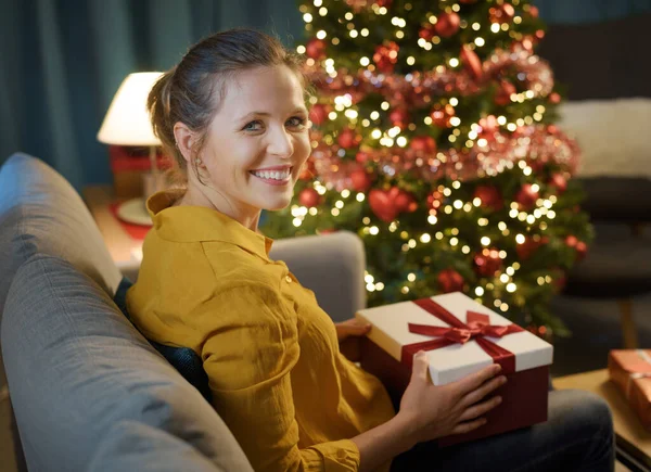 快乐的女人坐在沙发上 拿着圣诞礼物 对着摄像机笑着 — 图库照片