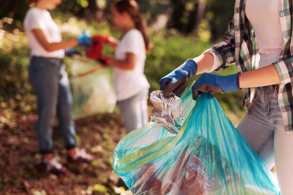 Volunteers cleaning up the park, a woman is putting trash in a garbage bag and some kids are helping her, environmental protection concept