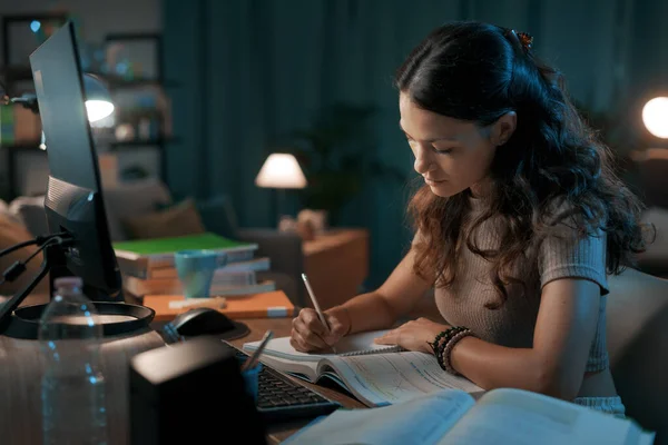 夜遅く家で宿題をしている若い学生は 彼女はノートに書いている — ストック写真