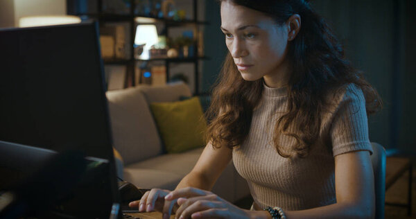 Сосредоточенная молодая женщина сидит за столом дома и работает допоздна