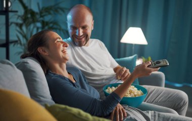 Evdeki kanepede oturan mutlu çift komik bir komedi filmi izleyip patlamış mısır yiyorlar.