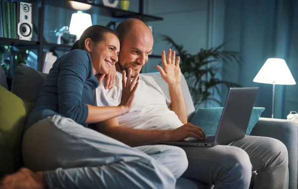幸せなカップル座っているソファとビデオ通話彼らのラップトップを使用してオンライン — ストック写真