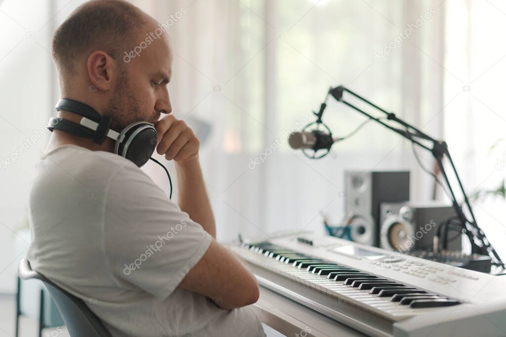 Professional musician sitting at desk and looking at the keyboard, he is composing a new song