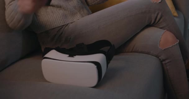 Mujer joven sentada en el sofá y accediendo a VR — Vídeo de stock