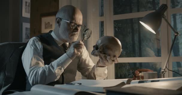 Professor sitting at desk and checking a human skull — Stock Video