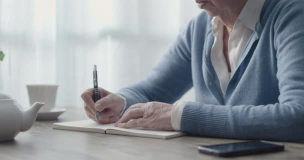 Oudere vrouw die op een notitieboekje schrijft — Stockvideo