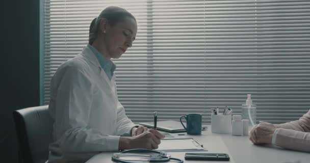 Medicul scrie o rețetă medicală pentru un pacient în vârstă — Videoclip de stoc