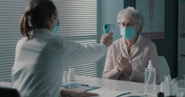 Лікар перевіряє температуру тіла пацієнта за допомогою інфрачервоного термометра — стокове відео