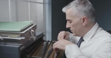 Şirket işadamı dosya dolabında dosya arıyor.