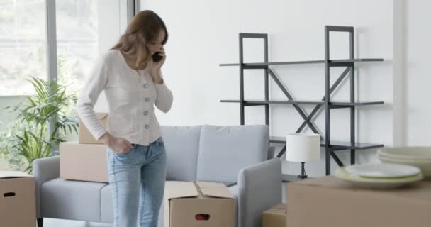 Woman moving in her new home and using her smartphone — Stock Video