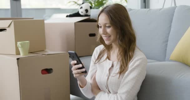Mujer moviéndose en su nuevo hogar y utilizando su teléfono inteligente — Vídeos de Stock