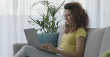 Kanepede oturan ve dizüstü bilgisayarında yazan bir kadın.