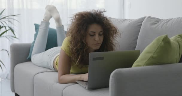 Donna sdraiata sul divano e utilizzando il suo computer portatile — Video Stock