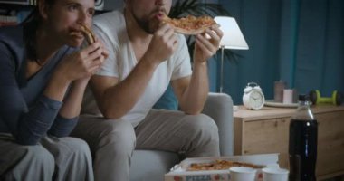 Mutlu çift kanepede oturup pizza yiyor.