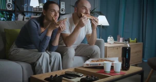 Ευτυχισμένο ζευγάρι κάθεται στον καναπέ και τρώει πίτσα — Αρχείο Βίντεο