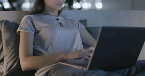 Mujer sentada en la cama y escribiendo con su portátil — Vídeo de stock