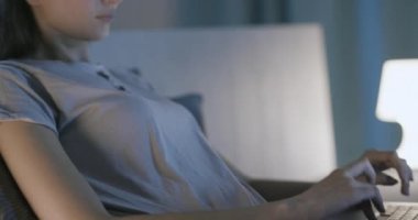 Yatakta oturmuş laptopuyla yazı yazan bir kadın.