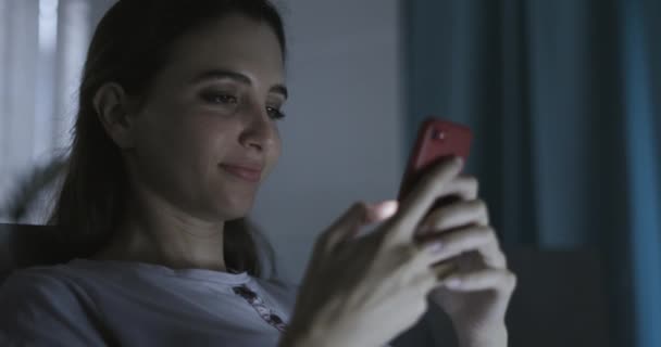 Frau sitzt im Bett und chattet mit ihrem Smartphone — Stockvideo