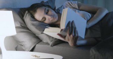 Yatakta dinlenen ve kitap okuyan bir kadın.