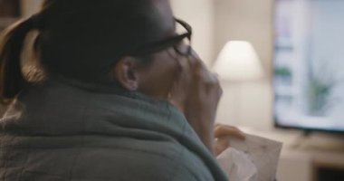 Üşütmüş ve grip olmuş bir kadın televizyon izliyor.