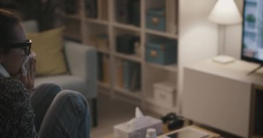 Üşütmüş ve grip olmuş bir kadın televizyon izliyor.