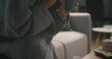 Grip olmuş bir kadın evde çay içiyor.