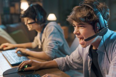 Young gamers sitting at desk and playing online video games together, one is shouting into the microphone