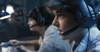 Friends playing online multiplayer videogames together, they are wearing headsets and staring at the computer screen