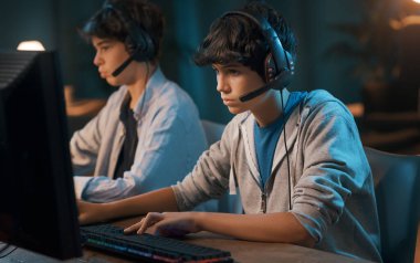 Teenager friends playing online video games together, they are wearing headsets and staring at the computer monitor