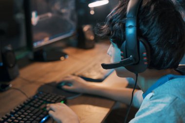 Young gamer wearing a headset and playing online multiplayer video games on his computer, entertainment and leisure concept