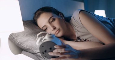 Young sleepless woman lying in bed at night and checking the time