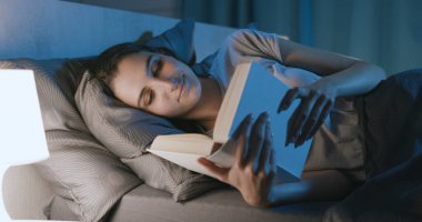 Young woman relaxing in her bed and reading a book at night