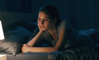 Worried young woman lying on bed at night, she is thinking and she is unable to sleep